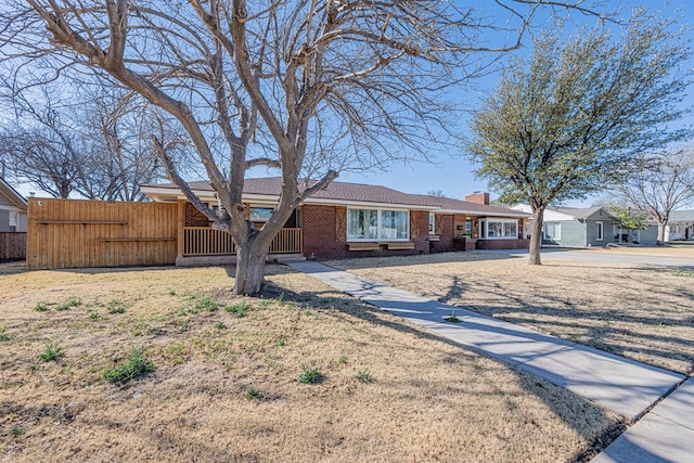 single story home with brick siding, a chimney, a front yard, and fence