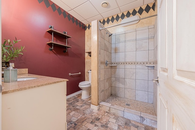 full bathroom with toilet, baseboards, tiled shower, and vanity