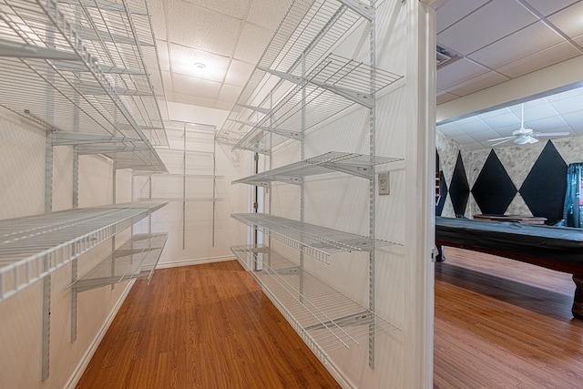 spacious closet featuring a drop ceiling, ceiling fan, billiards, and wood finished floors