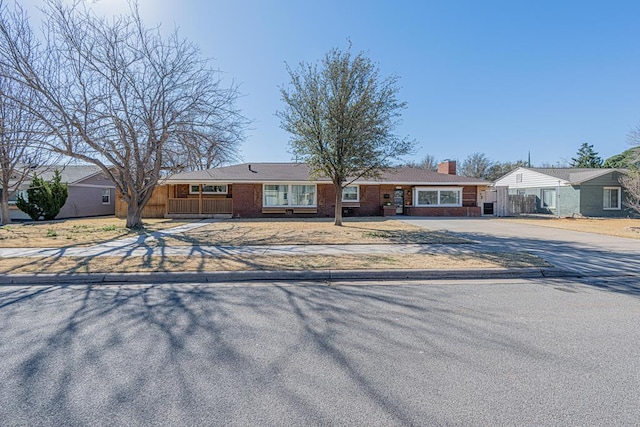 view of front of property with driveway, brick siding, a chimney, and fence