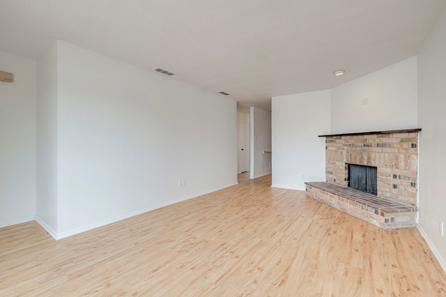 unfurnished living room with a fireplace, wood finished floors, visible vents, and baseboards