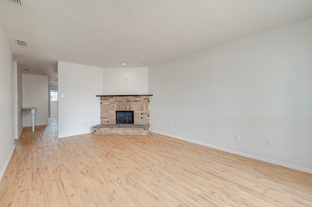 unfurnished living room with a brick fireplace, light wood-style flooring, visible vents, and baseboards