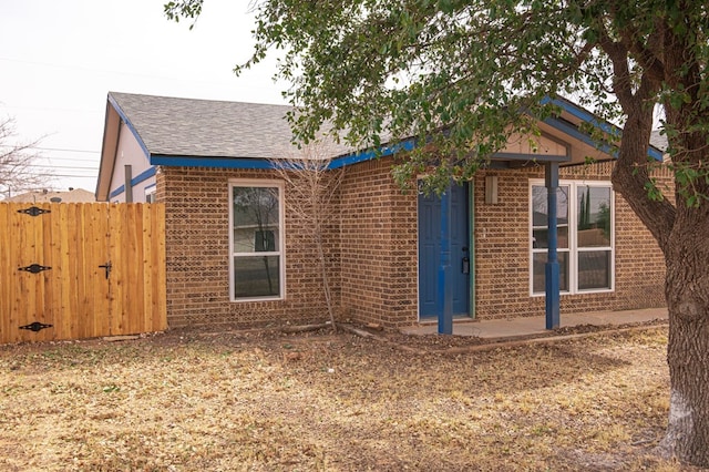 view of front of property featuring brick siding, a shingled roof, and fence