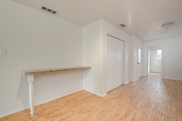 spare room with light wood-type flooring, visible vents, and baseboards