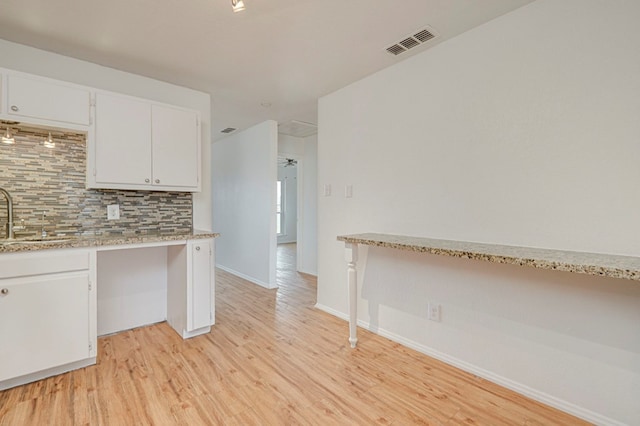 kitchen with a sink, white cabinetry, visible vents, light wood-style floors, and backsplash