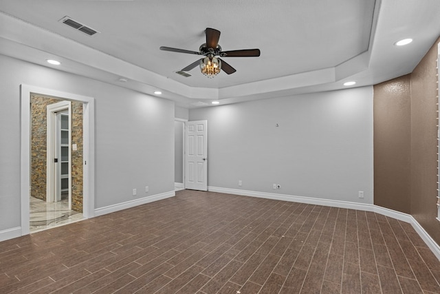 empty room with a tray ceiling, wood-type flooring, and ceiling fan