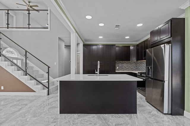 kitchen featuring sink, appliances with stainless steel finishes, dark brown cabinets, tasteful backsplash, and a center island with sink