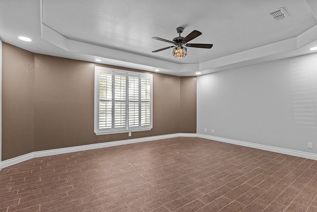 empty room with ceiling fan, a raised ceiling, and hardwood / wood-style floors