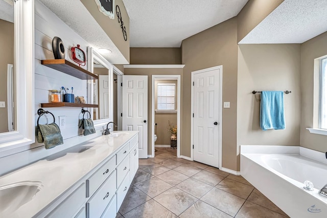full bathroom with toilet, healthy amount of natural light, a bath, a textured ceiling, and double vanity
