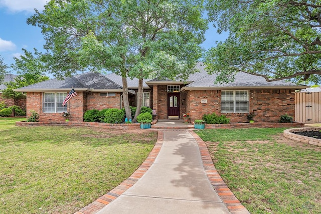 single story home featuring brick siding, a front yard, and roof with shingles