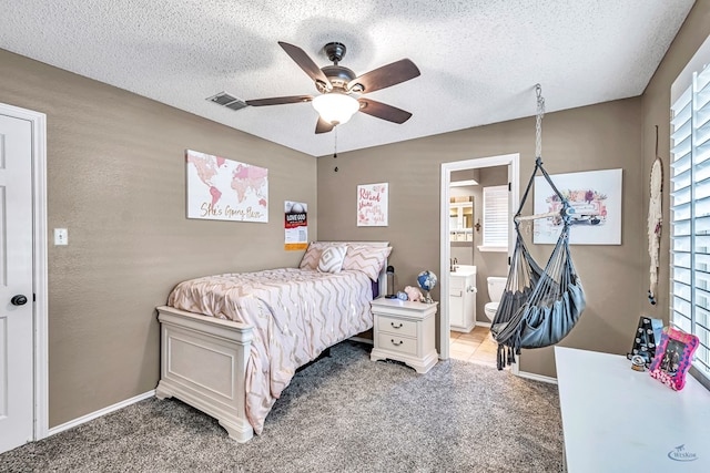 bedroom featuring light carpet, a textured ceiling, multiple windows, ceiling fan, and ensuite bath