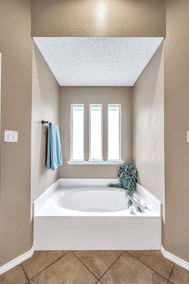 bathroom with tile patterned flooring, a bath, baseboards, a textured wall, and a textured ceiling