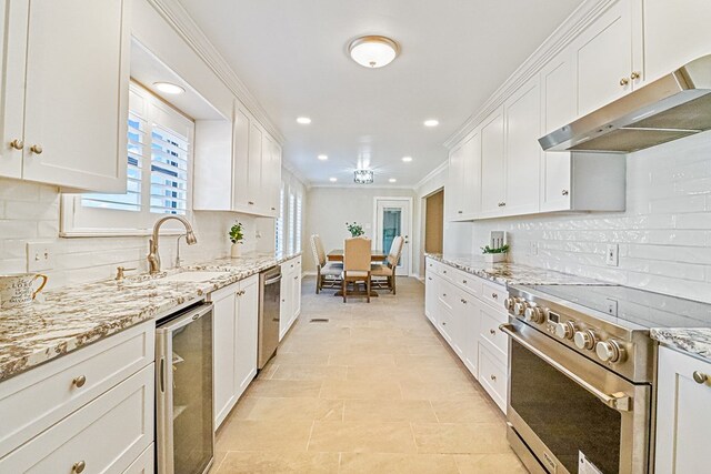 kitchen with light stone countertops, backsplash, stainless steel appliances, crown molding, and white cabinetry