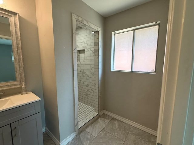 full bath featuring a tile shower, vanity, baseboards, and marble finish floors