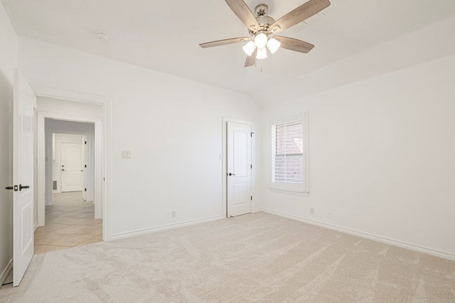 spare room with a ceiling fan, light colored carpet, vaulted ceiling, and baseboards