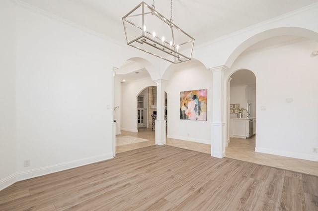 unfurnished dining area with arched walkways, a sink, baseboards, light wood finished floors, and crown molding