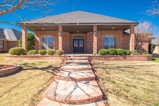 view of front of property featuring french doors, a front lawn, a shingled roof, and brick siding