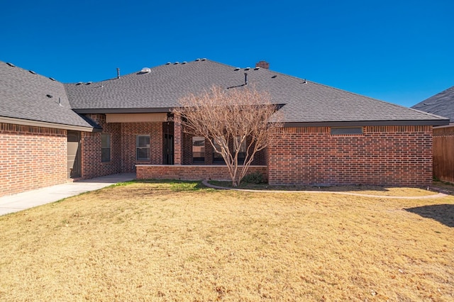 rear view of property with brick siding, a lawn, a shingled roof, and fence