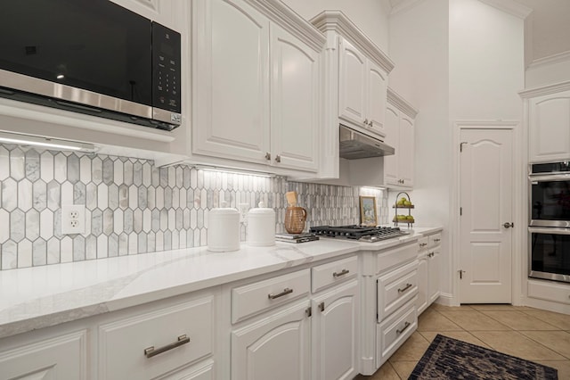 kitchen with light tile patterned floors, under cabinet range hood, stainless steel appliances, white cabinets, and light stone countertops