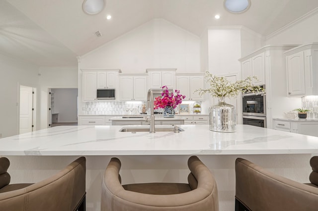 kitchen with double oven, a spacious island, white cabinetry, and built in microwave