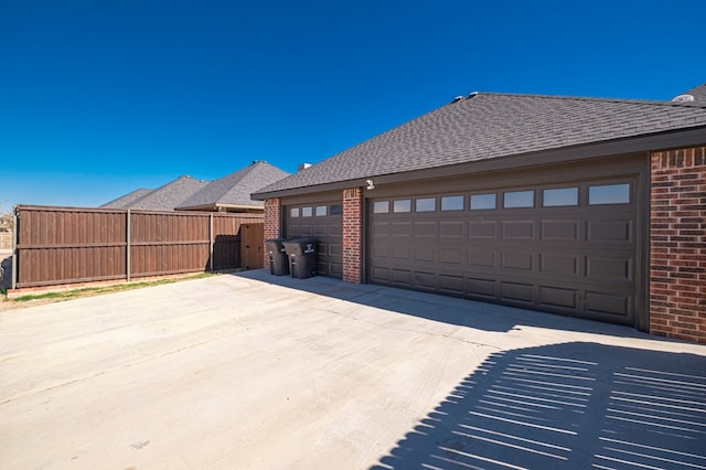 exterior space with a garage, brick siding, fence, and roof with shingles