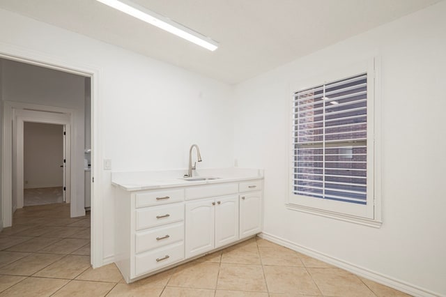 kitchen with light tile patterned flooring, a sink, baseboards, white cabinets, and light countertops