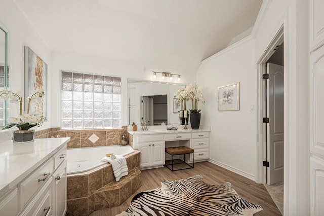 bathroom with a garden tub, ornamental molding, wood finished floors, and vanity