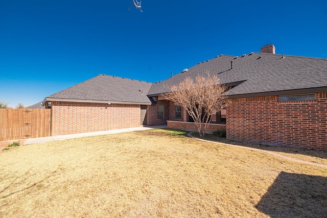 rear view of property with a chimney, fence, and brick siding