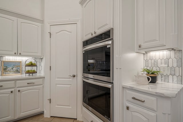 kitchen featuring light tile patterned floors, stainless steel double oven, decorative backsplash, and white cabinets