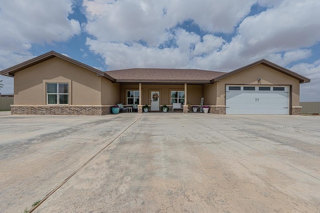 single story home featuring a porch, stucco siding, brick siding, a garage, and driveway