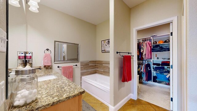 full bathroom with vanity, baseboards, a bath, tile patterned floors, and a spacious closet