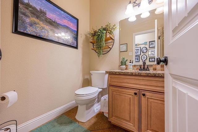 bathroom with baseboards, toilet, a textured wall, and vanity