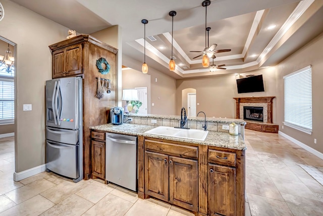 kitchen with appliances with stainless steel finishes, pendant lighting, sink, a raised ceiling, and a brick fireplace