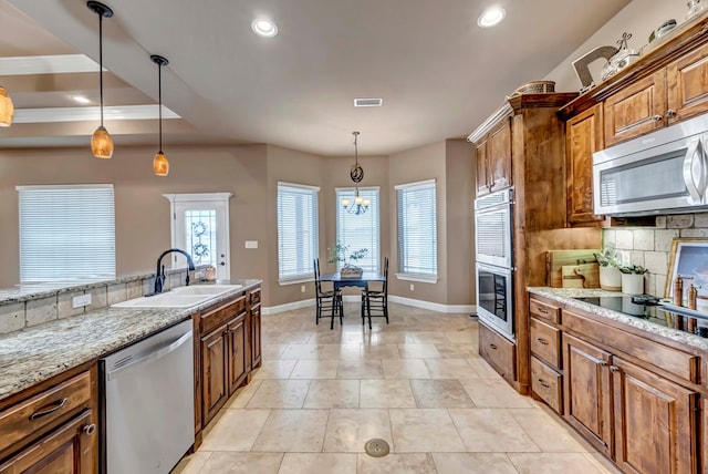 kitchen featuring sink, backsplash, hanging light fixtures, stainless steel appliances, and light stone counters