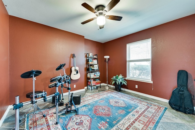 exercise area with ceiling fan, a textured wall, and baseboards