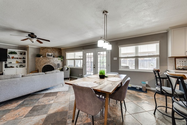 dining space with a textured ceiling, baseboards, ornamental molding, french doors, and a brick fireplace