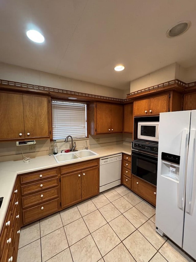 kitchen featuring a sink, light tile patterned floors, white appliances, and brown cabinets