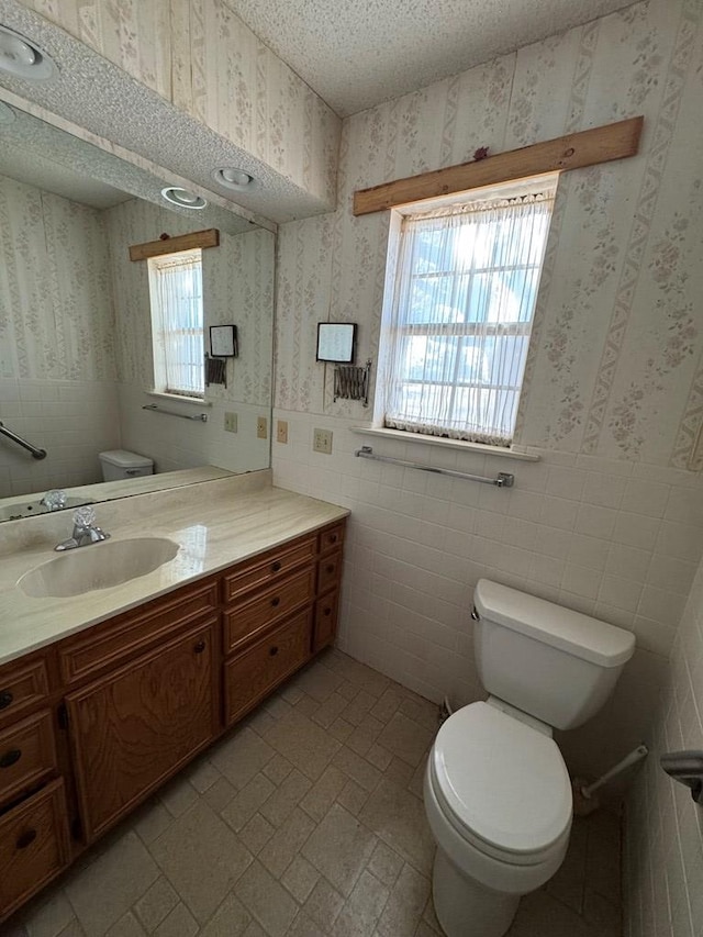 bathroom with toilet, wallpapered walls, a textured ceiling, and wainscoting