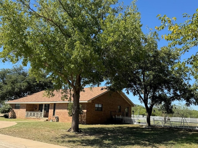 view of home's exterior featuring fence, a porch, a lawn, and brick siding