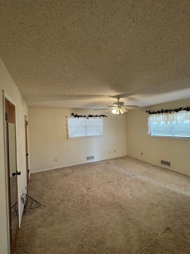 unfurnished room with light carpet, a textured ceiling, visible vents, and a ceiling fan