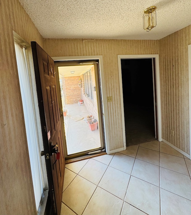 doorway featuring light tile patterned floors, a textured ceiling, and wallpapered walls