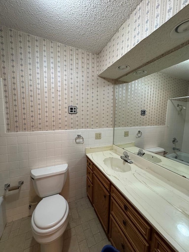 bathroom featuring a wainscoted wall, a textured ceiling, toilet, and wallpapered walls