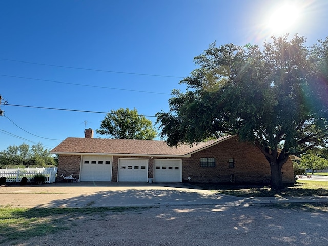 view of front of property with an attached garage, brick siding, fence, driveway, and a chimney