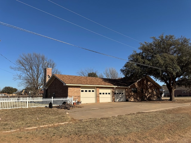 view of side of property featuring concrete driveway, a chimney, brick siding, a garage, and fence