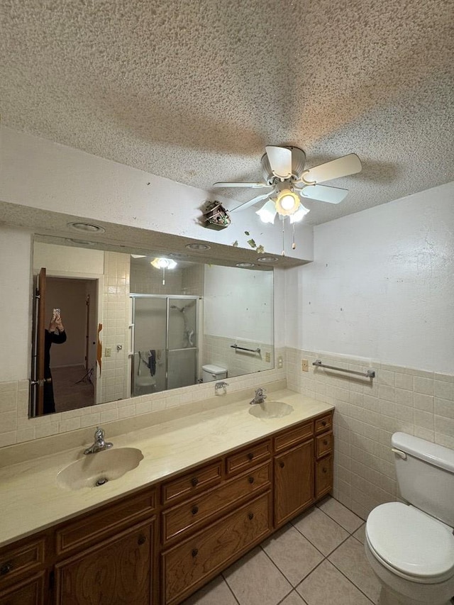 full bath with toilet, a stall shower, a sink, and tile walls