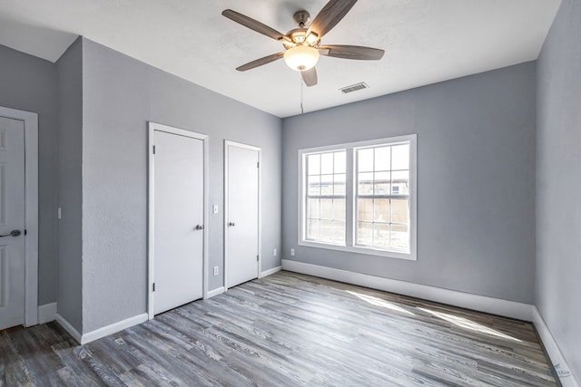 unfurnished bedroom featuring two closets, ceiling fan, and hardwood / wood-style flooring