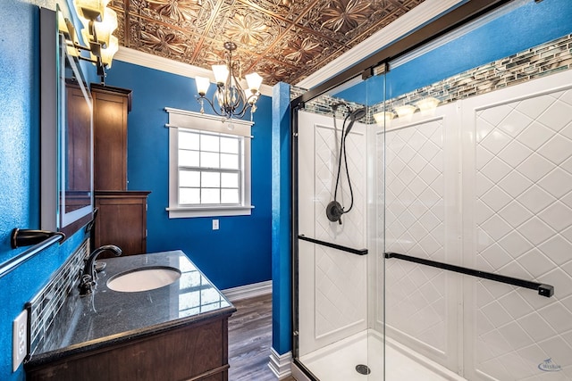 bathroom with an inviting chandelier, hardwood / wood-style floors, an enclosed shower, vanity, and ornamental molding