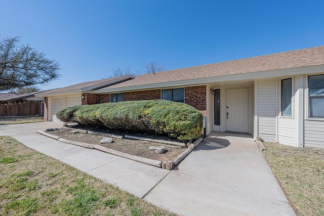 single story home with a shingled roof, brick siding, fence, and an attached garage