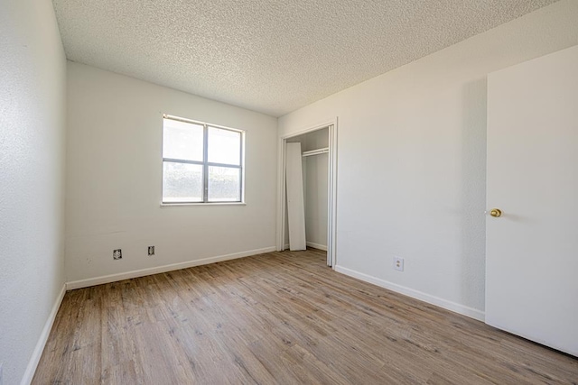 unfurnished bedroom featuring a closet, a textured ceiling, baseboards, and wood finished floors