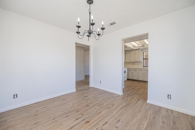 unfurnished dining area featuring a textured ceiling, a chandelier, visible vents, baseboards, and light wood finished floors